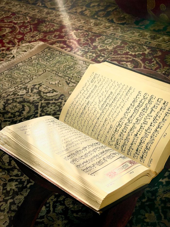 Open Quran with Arabic text illuminated by sunlight on an ornate carpet, symbolizing spirituality.