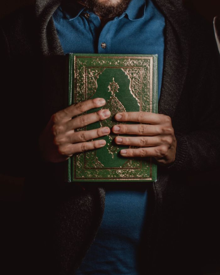 Crop unrecognizable ethnic bearded male in casual clothes holding religious holy Quran in hands