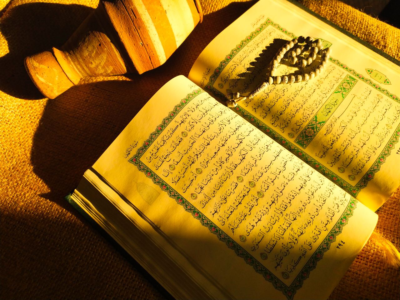 An open Quran with prayer beads and pottery, bathed in warm sunlight. Perfect for religious or cultural content.